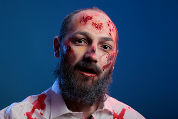 Portrait of undead scary zombie man posing with bloody scars and spooky halloween costume looking...