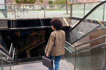 rear view of a successful business woman entering to the subway station with her briefcase, concept...