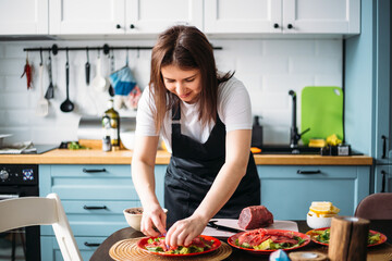  A young attractive girl in an apron prepares carpaccio in the home kitchen.