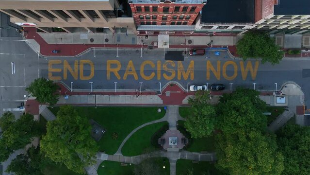 End Racism Now slogan painted on city street in USA. Rising aerial. BLM Black Lives Matter, George Floyd theme.