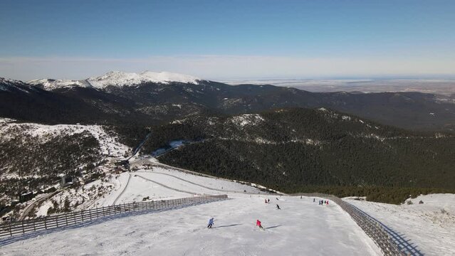 Stabilized shot of a snowy mountain side while people are skiing on a sunny winter day.