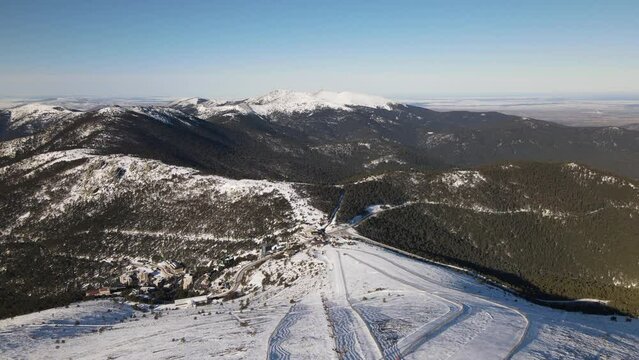 Rising aerial establishing shot over a ski track on the top of a snowy mountain.