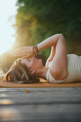 A mindful woman is lying on her back and holding hands in a namaste position while practicing...