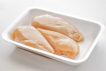 Raw chicken breast fillet on a white foam meat tray on white background.