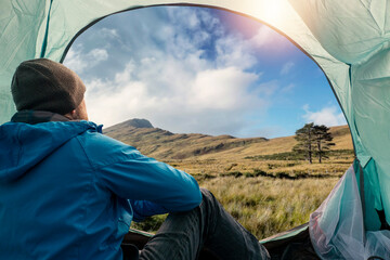 Male tourist sitting in a tent and looking out at stunning nature landscape with fields and...