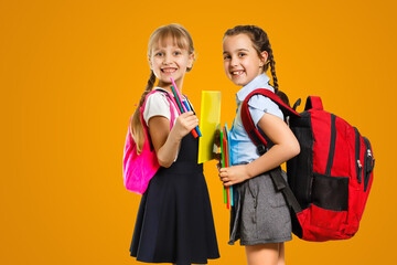 Education Concept. Set portrait of diverse schoolchildren holding stack of academic books and wearing backpack, yellow orange color studio background