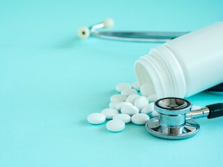 White tablets or multivitamins are poured out of a plastic jar on a blue, stethoscope, a place for text. The concept of healthcare and health care
