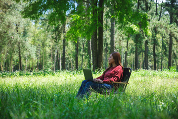 A beautiful asian woman working and typing on laptop keyboard while sitting on a chair in the park