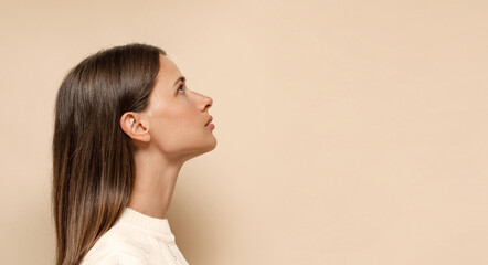 Caucasian female with long shiny hair with nude makeup in profile on a beige background