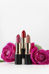 Obraz na płótnie Canvas Set colourful lipstick with pink roses on white background. Still life of glamour lipstick, decorative cosmetics.