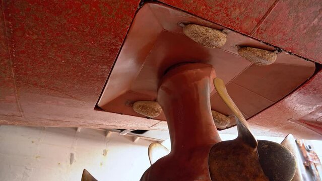 Azimuth foundation in bottom of ships hull seen from insode drydock - Clip slowly rotating around propeller while looking up at foundation with zinc anodes - Dirty hull before cleaning