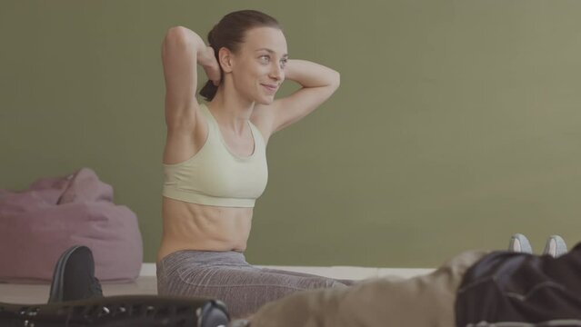 Slowmo of young female sports trainer doing crunches on mat while showing exercise to man with prosthetic leg