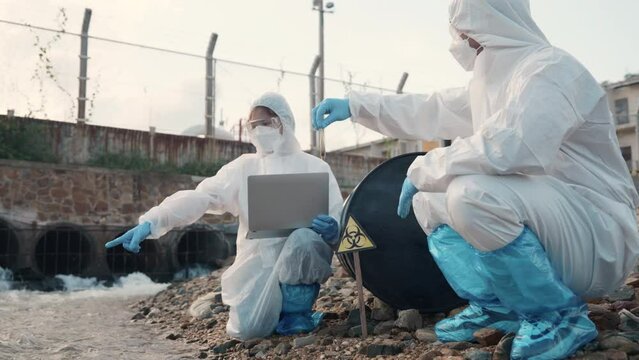 Ecologist sample water from the river and get fishes dead to check effected case in laboratory, Biologist wear protect suit and mask collects sample of waste water from industrial, problem environment