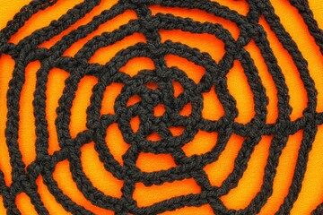 Black crochet spider web on orange background with copy space for text. Halloween autumn decoration scary creepy horror concept. Idea for banner, postcard, poster. Spooky Cobweb. Flat lay, mock up
