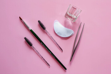 Materials for depilation of eyebrows on a pink background. Wooden stick for wax, brushes, brush for coloring, tweezers