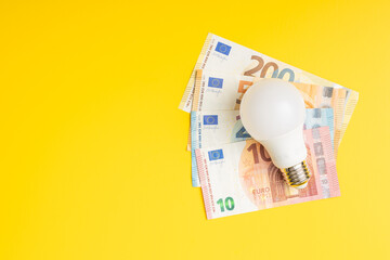 Light bulb and euro on yellow background. Concept of increasing electric prices.