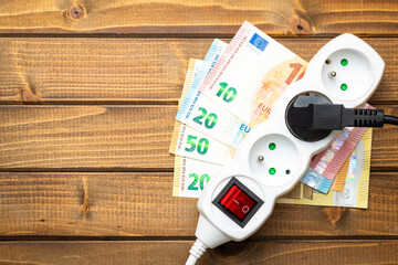 Electric socket and euro money on wooden table. Concept of increasing electric prices.
