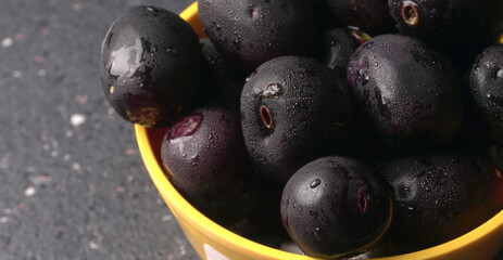 Jambul or Jamun (Syzygium cumini) in yellow bowl isolated on textured background.