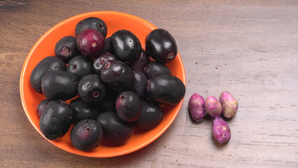 Jambul or Jamun (Syzygium cumini) in yellow bowl isolated on textured background.