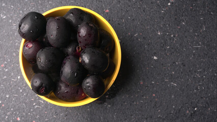 Jambul or Jamun (Syzygium cumini) in yellow bowl isolated on textured background.