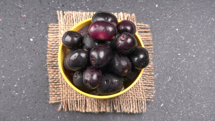 Jambul or Jamun (Syzygium cumini) in yellow bowl isolated on textured background.