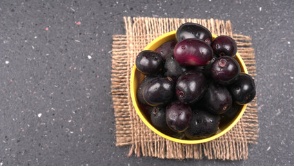 Jambul or Jamun (Syzygium cumini) in yellow bowl isolated on textured background.