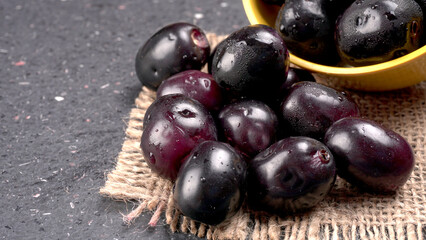 Jambul or Jamun (Syzygium cumini) in yellow bowl isolated on textured background.