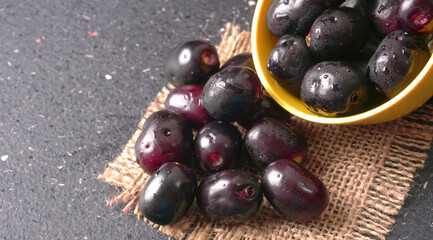 Jambul or Jamun (Syzygium cumini) in yellow bowl isolated on textured background.