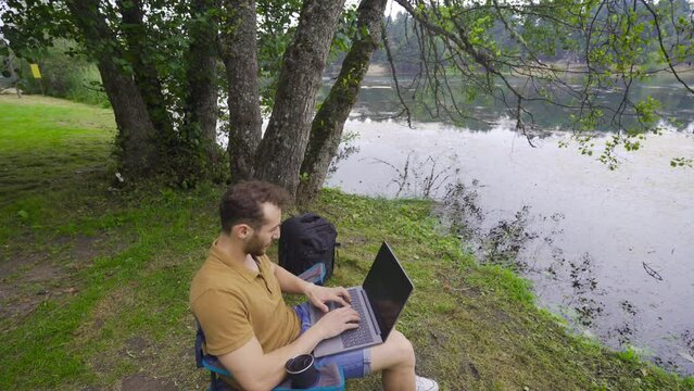 Freelance businessman working on laptop in nature park.
Businessman sits in his chair in the forest and works with a laptop.
