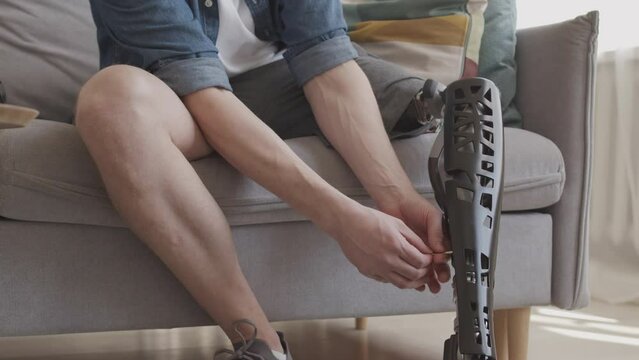 Cropped slowmo of unrecognizable man assembling prosthesis onto his leg while sitting on sofa at home
