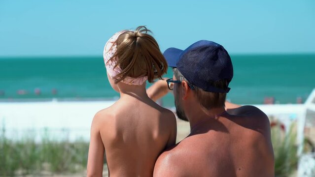 Back view of father and girl look at hotel beach with blue sea. Concept of summer vacation, travel, holiday. People outdoors on seascape