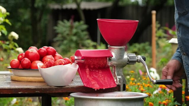Tomato juice. Squeezing tomato juice with juice squeezing machine. Tomatoes are processed into tomato juice in a juicer at home outdoors. Tomatoes in a meat grinder in summer day
