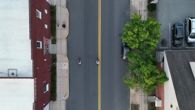 Boys ride bikes on city street in downtown USA. Top down aerial in residential housing area.