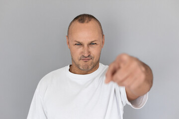 Portrait of determined mature man pointing at camera. Balding Caucasian guy wearing white T-shirt looking at camera and stretching his arm. Choosing you concept