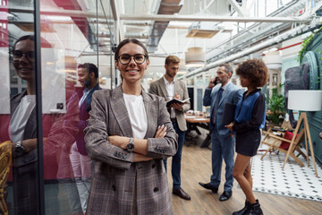 Portrait of smiling businesswoman standing in modern office on colleagues background