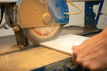 Worker hand cutting ceramic tile with water cutting machine close-up. Circular saw for tile...