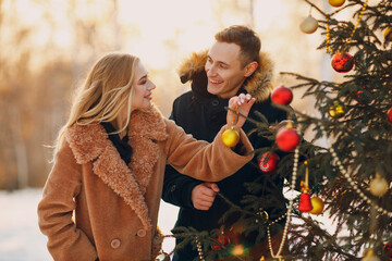 Young adult couple decorates christmas tree in winter forest. New year pine holiday party...
