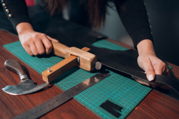 Tanner woman cutting leather goods on workshop. Working process of leather craftsman.