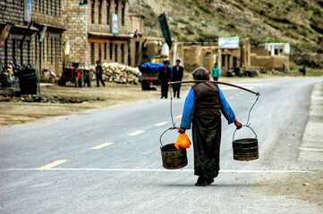 Elderly woman struggling to carry buckets of water