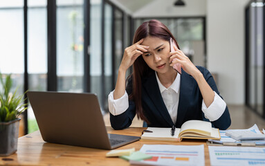 Young serious office worker female sitting at desk at workplace holding mobile phone makes business call listens client claims feels displeased annoyed and anxious, problems at work concept