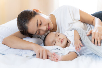 Obraz na płótnie Canvas Mom and Newborn,Happy family concept.Close up view of beautiful Asian mother and her sleeping newborn baby.Mother holding baby hand in one hand and holding hand the baby with eyes closing and smiling.