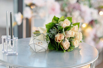A pair of beautiful wedding rings in a modern glass stand and a delicate bridal bouquet of roses. Marriage, ceremony. Soft selective focus.
