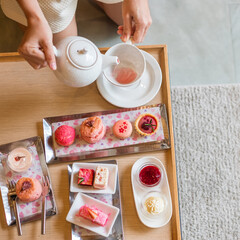 Woman hand pouring hot tea with Afternoon tea set and Pink dessert at luxury hotel