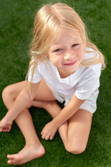 Fototapeta premium Portrait pretty smiling blonde girl sitting on green grass. Mock up white t shirt. Top view.