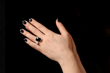 clasped woman hands with black manicure and stylish ring on finger on dark background