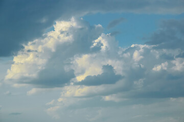 Picturesque sky with thunderstorms cumulus clouds at sunset. Blue sky with big clouds, backlit by sun. Air clouds background. Copy space. Selective focus.