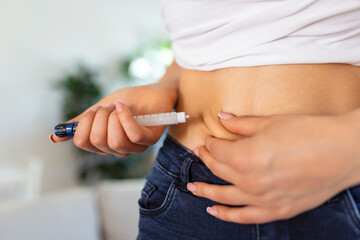 A diabetic patient using insulin pen for making an insulin injection at home. Young woman control...