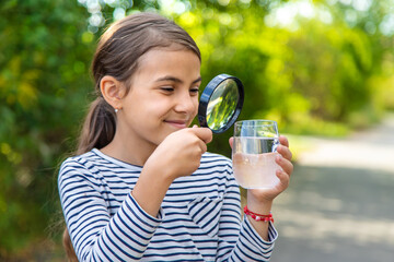 The child examines the water with a magnifying glass. Selective focus.