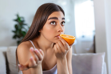 Sick woman trying to sense smell of half fresh orange, has symptoms of Covid-19, corona virus infection - loss of smell and taste. One of the main signs of the disease. - obrazy, fototapety, plakaty