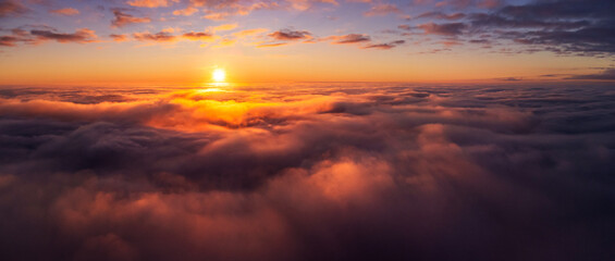 Majestic photo above the clouds of setting sun under horizon. Vibrant colours of burning clouds lit by last sun rays
